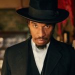 Benjamin Zephaniah wearing a black hat and outfit looking at the camera.