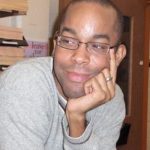 Christopher M. Bell wearing a gray pull over sweat shirt looking to his right.