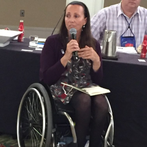 Candace Cable wearing a purple sweater while speaking as she sits in from of a table.