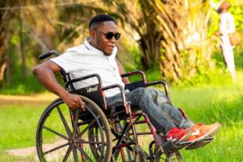 A guy in a wheelchair outside and surrounded trees and grass.